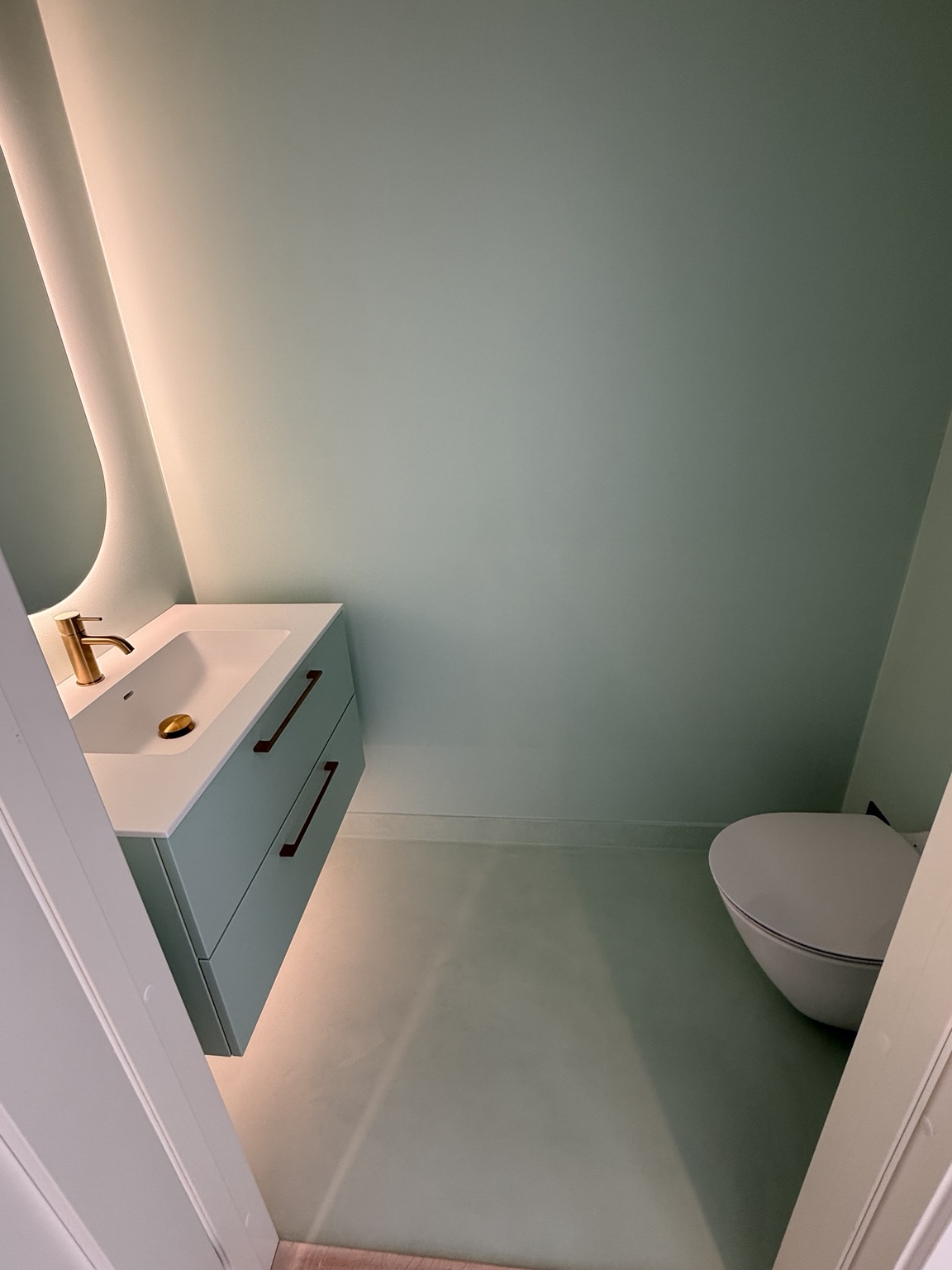 Grönt badrum med microcement, handfat och toalett